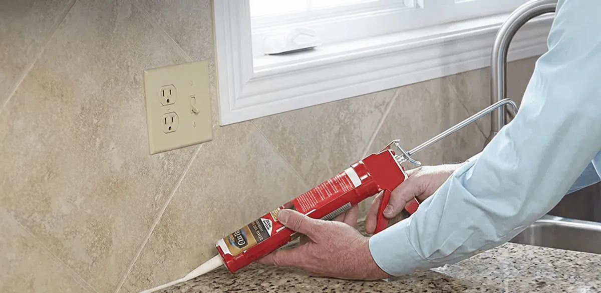 Handyman applying caulk along a kitchen backsplash and countertop seam in Peoria, IL