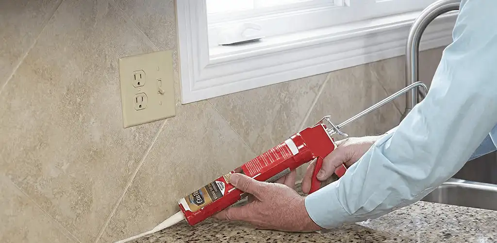 Handyman applying caulk along a kitchen backsplash and countertop seam in Peoria, IL